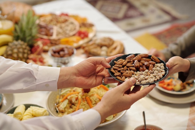 Hombre irreconocible pasando plato con nueces a un pariente durante la cena