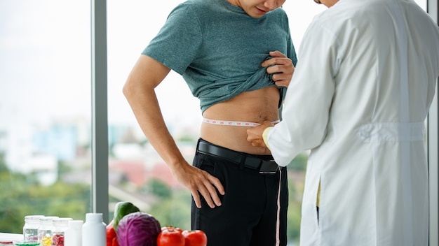 Hombre irreconocible en uniforme médico midiendo la cintura del paciente masculino de cultivo durante el trabajo en la clínica