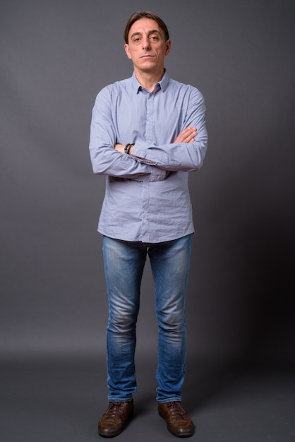 Foto hombre italiano guapo maduro con camisa azul contra la pared gris