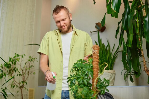 Hombre jardinero rociado riego Schefflera olla en el hogar el cuidado de las plantas de interior vegetación en el hogar amor de las plantas jardín acogedor interior