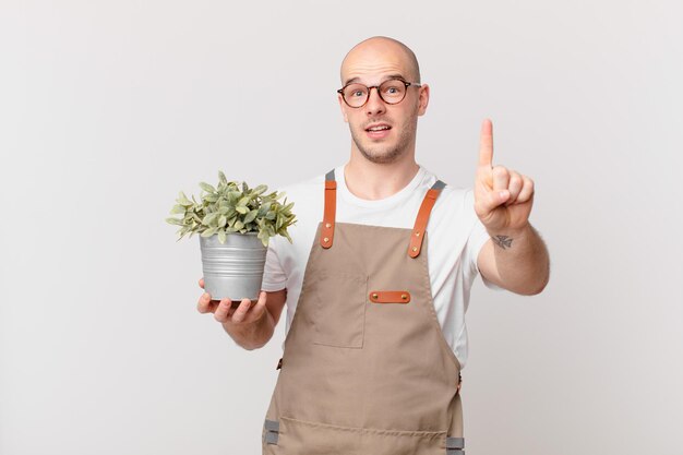 Hombre jardinero sonriendo con orgullo y confianza haciendo la pose número uno triunfalmente, sintiéndose como un líder