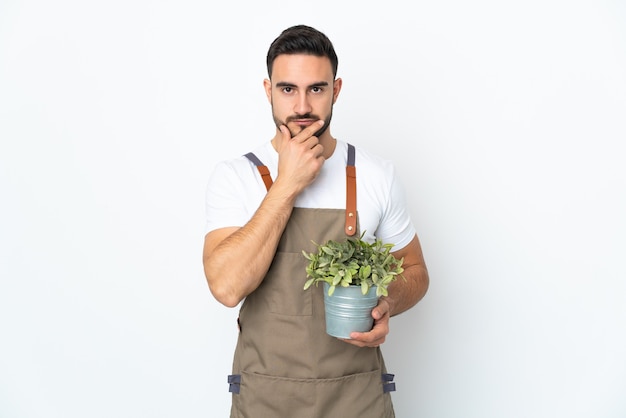 Hombre jardinero sosteniendo una planta aislada sobre fondo blanco pensando