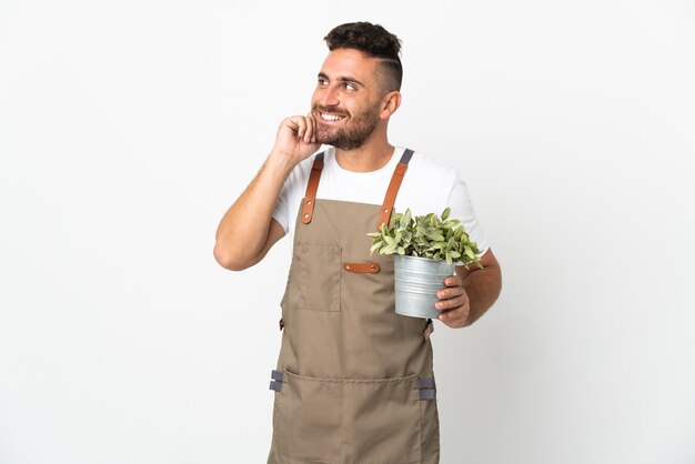 Hombre jardinero sosteniendo una planta sobre blanco aislado pensando en una idea mientras mira hacia arriba