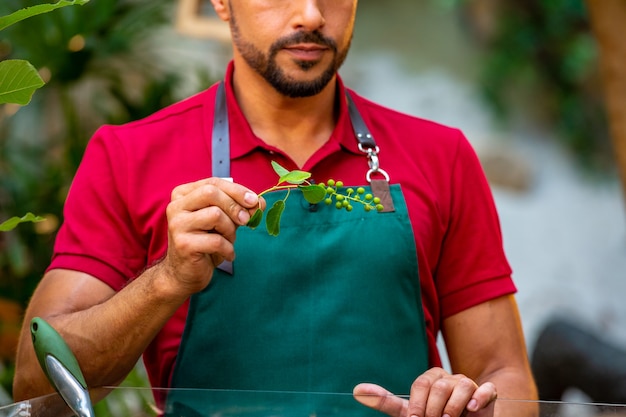 Hombre jardinero sosteniendo una rama con bayas verdes en sus manos