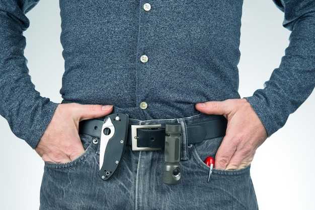 Hombre en jeans en un cinturón de cuero con una linterna y un cuchillo artículos de supervivencia