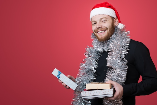 Hombre de jengibre con gorro de Papá Noel está anunciando algo mientras sostiene el regalo de año nuevo en la pared roja