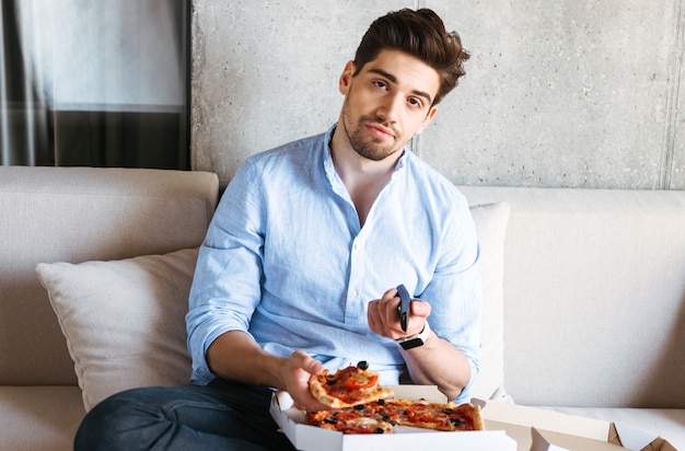 Foto hombre joven aburrido sosteniendo el control remoto de la tv