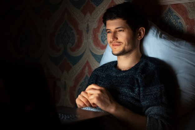 Hombre joven acostado en casa y mirando en la computadora portátil.