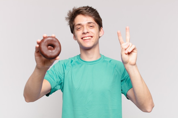 Hombre joven adolescente celebrando una victoria exitosa y sosteniendo una rosquilla