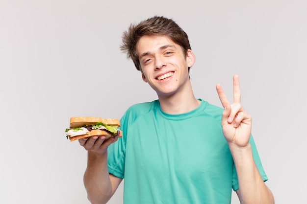 Hombre joven adolescente celebrando una victoria exitosa y sosteniendo un sándwich