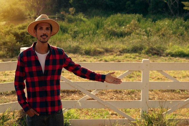 Hombre joven agricultor negro apuntando en tierras de cultivo African Ayoung hombre con sombrero en la granja con puesta de sol