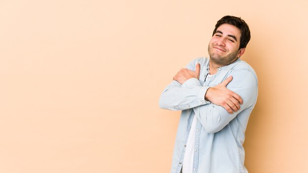 Hombre joven aislado en abrazos beige, sonriendo despreocupado y feliz.