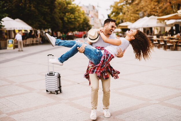 Hombre joven alegre con gafas de sol y sombrero con hermosa chica en brazos.