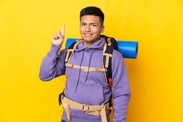 Hombre joven alpinista con una gran mochila aislada sobre fondo amarillo apuntando hacia una gran idea
