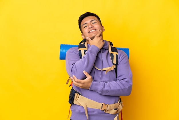 Hombre joven alpinista con una gran mochila aislada sobre fondo amarillo feliz y sonriente