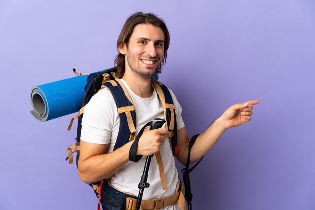 Hombre joven alpinista con una gran mochila sobre antecedentes aislados que señala el dedo hacia el lado