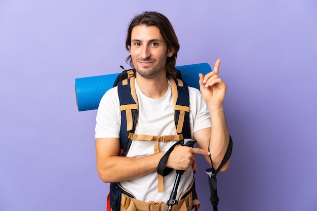 Hombre joven alpinista con una gran mochila sobre fondo aislado apuntando hacia una gran idea