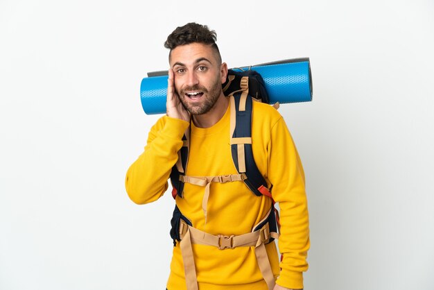 Hombre joven alpinista con una gran mochila sobre fondo aislado con sorpresa y expresión facial conmocionada