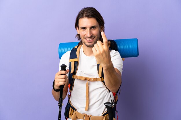 Hombre joven alpinista con una gran mochila sobre pared aislada haciendo gesto de venida