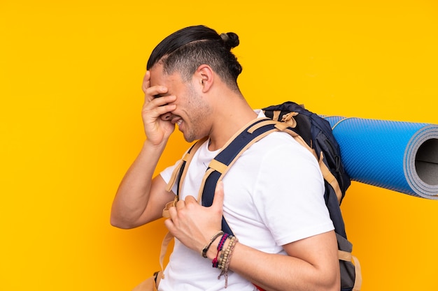 Hombre joven alpinista con una gran mochila sobre pared aislada