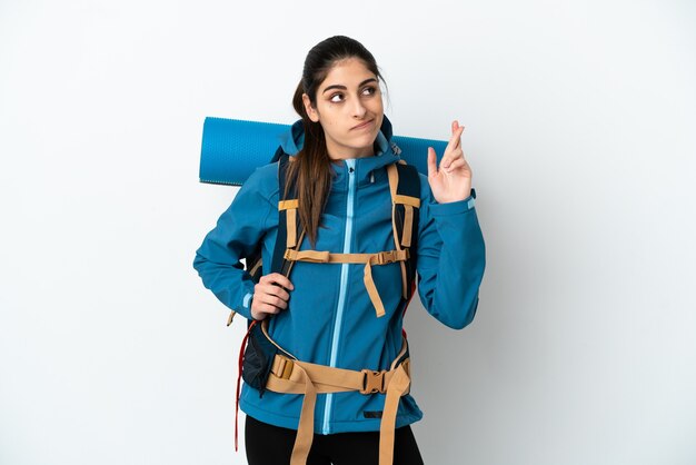 Foto hombre joven alpinista con una mochila grande sobre fondo aislado con los dedos cruzados y deseando lo mejor