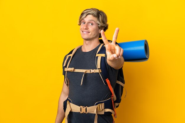 Hombre joven alpinista sobre amarillo aislado sonriendo y mostrando el signo de la victoria