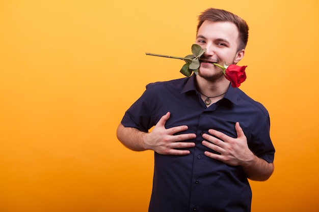 Hombre joven apasionado con rosa roja en la boca sobre fondo amarillo. amor joven