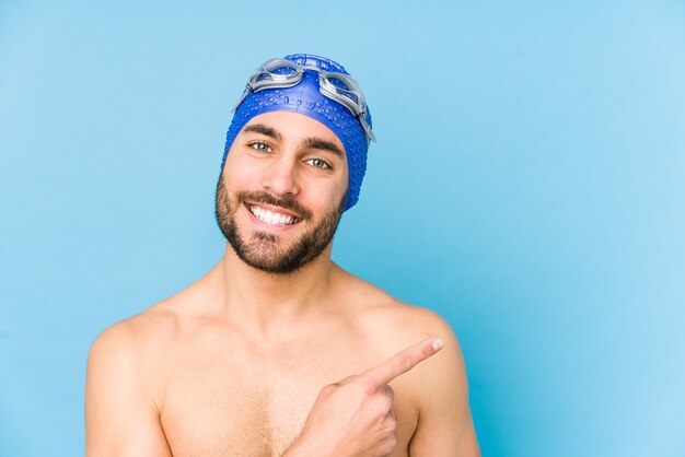 Hombre joven apuesto nadador aislado sonriendo y apuntando a un lado, mostrando algo en el espacio en blanco.