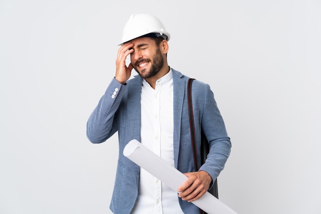 Hombre joven arquitecto con casco y sosteniendo planos aislados en blanco riendo