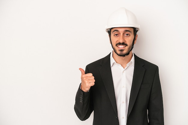 Hombre joven arquitecto que llevaba un casco de construcción aislado sobre fondo blanco sonriendo y levantando el pulgar hacia arriba