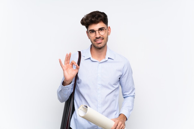 Hombre joven arquitecto sobre blanco aislado que muestra un signo bien con los dedos