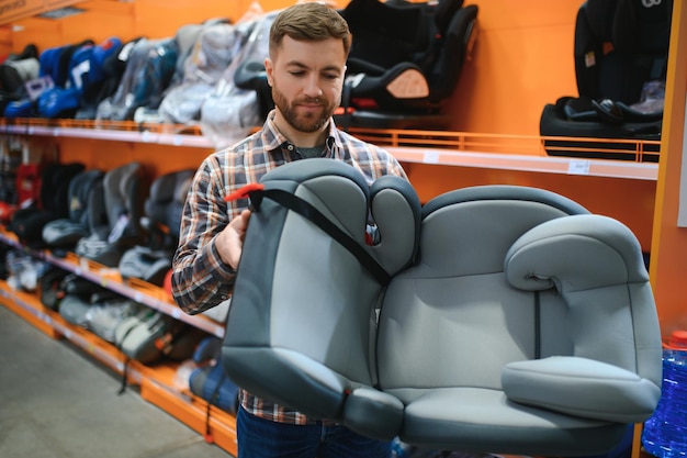 Hombre joven con asiento de coche para niños en la tienda infantil