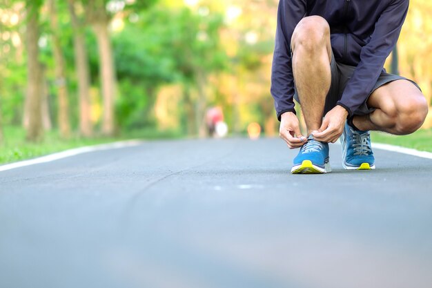 Hombre joven del atleta que ata las zapatillas deportivas en el parque al aire libre