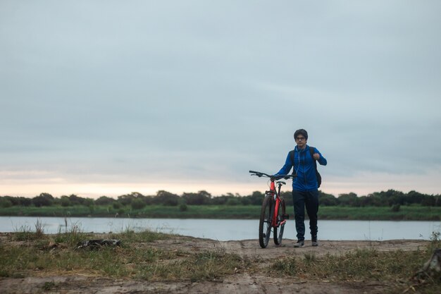 Hombre joven con auriculares caminando con su bicicleta junto a él