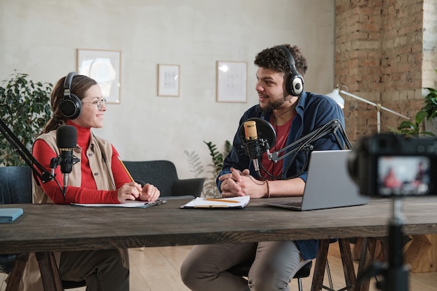 Hombre joven en auriculares entrevistando a una mujer en la mesa durante la transmisión en el estudio de radio