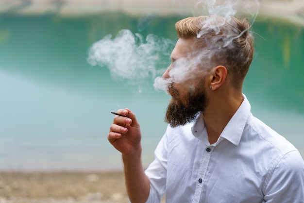 Hombre joven con barba fuma cigarrillo o tabaco. El chico es adicto a los cigarrillos y siempre fuma mucho t ...