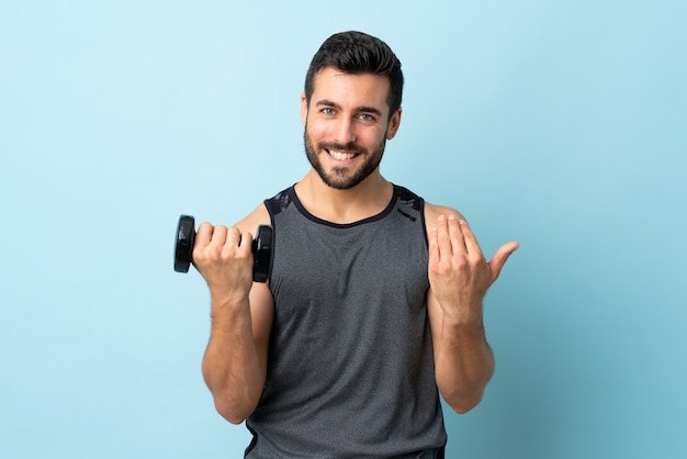 Hombre joven con barba haciendo levantamiento de pesas invitando a venir con la mano