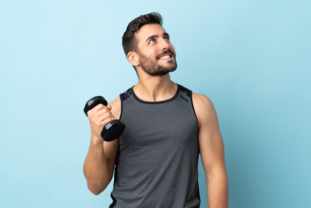 Hombre joven con barba haciendo levantamiento de pesas mirando hacia arriba mientras sonríe