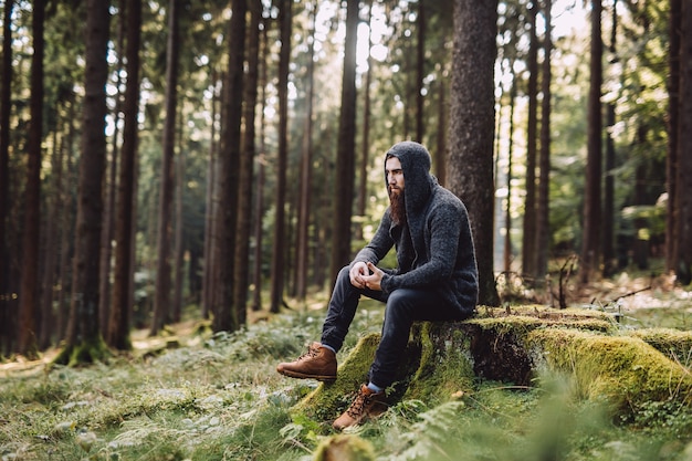 Hombre joven con barba sentado y piensa en el bosque