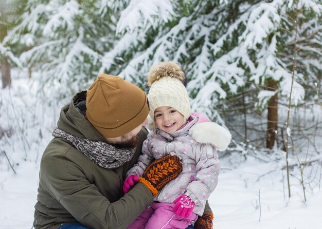 Hombre joven barbudo con niña divertirse en el bosque nevado en invierno