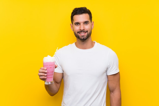 Hombre joven con batido de fresa sobre pared amarilla aislada sonriendo mucho