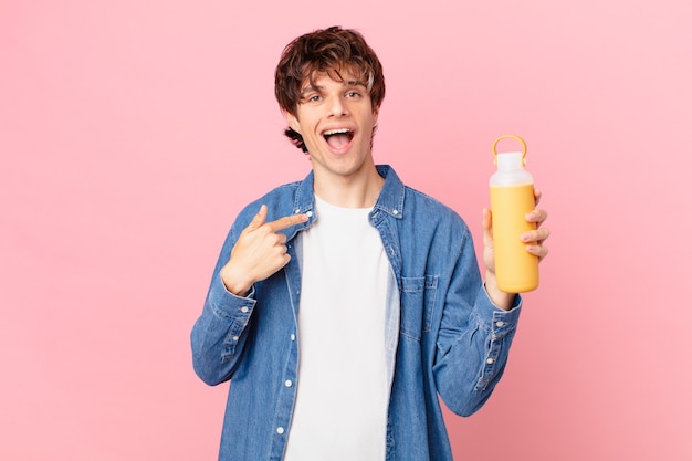 Hombre joven con un batido sintiéndose feliz y apuntando a sí mismo con un emocionado