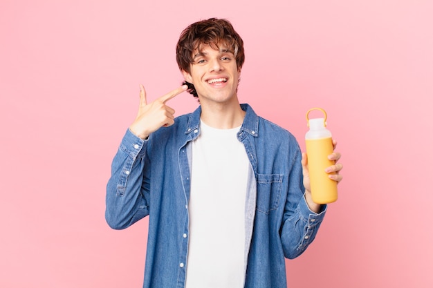 Hombre joven con un batido sonriendo con confianza apuntando a su propia sonrisa amplia