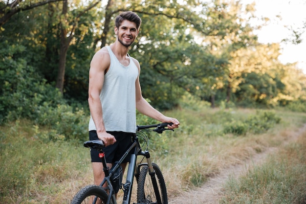 Hombre joven con bicicleta en el camino forestal mirando al frente