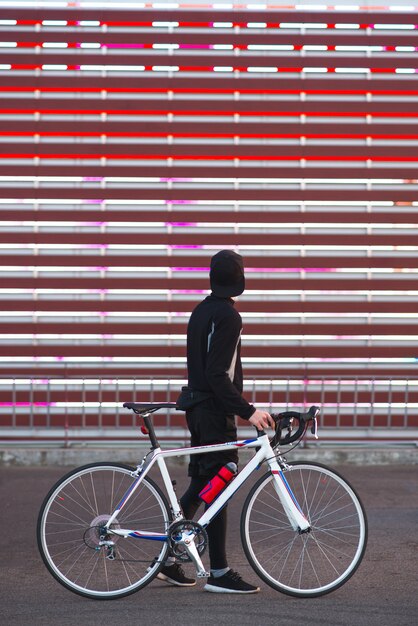 El hombre joven con una bicicleta y un vestido atlético está en un fondo rojo abstracto.