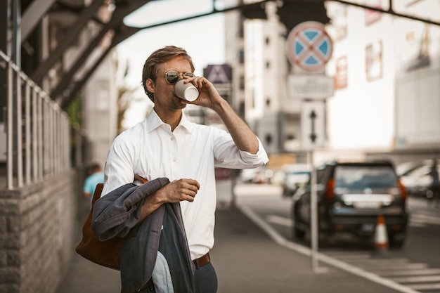 Hombre joven bien vestido tomando café al aire libre.