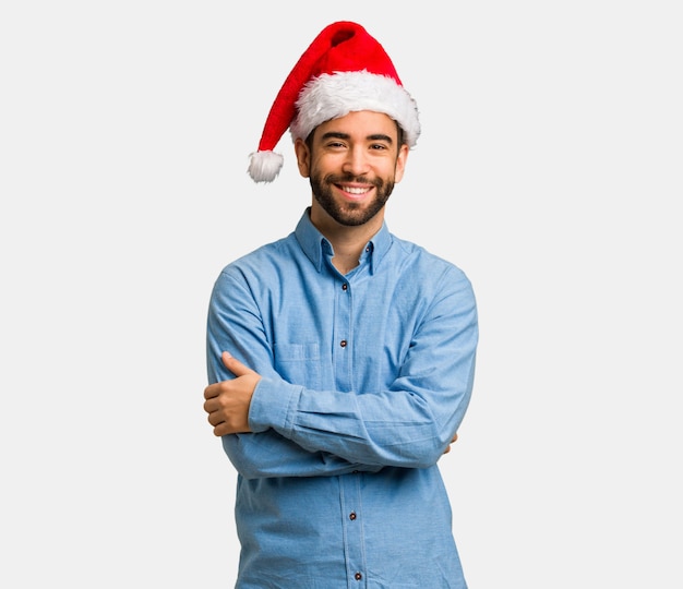 Hombre joven con los brazos de santa sombrero cruzando los brazos, sonriendo y relajado