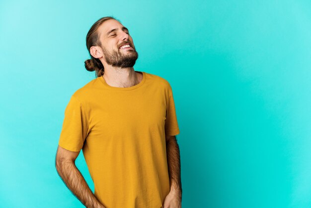 Hombre joven con cabello largo parece relajado y feliz riendo, cuello estirado mostrando los dientes.