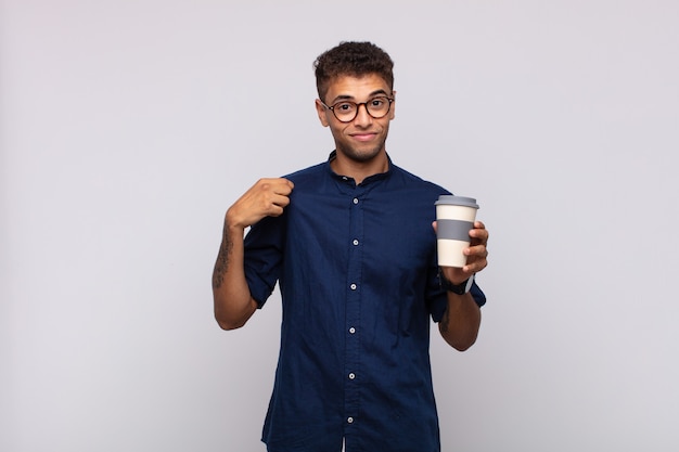 Hombre joven con un café que parece arrogante, exitoso, positivo y orgulloso, apuntando a sí mismo