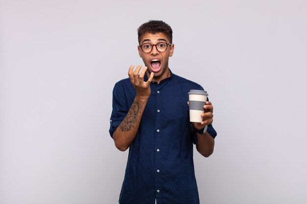 Hombre joven con un café que parece desesperado y frustrado, estresado, infeliz y molesto, gritando y gritando